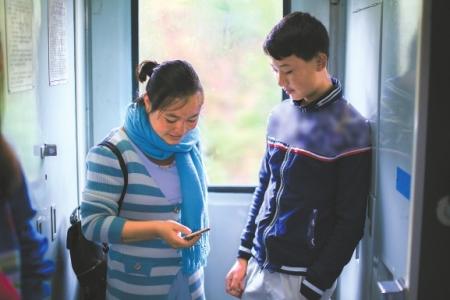  吉木呷呷在火车上用手机自学外语，旁边是她弟弟。