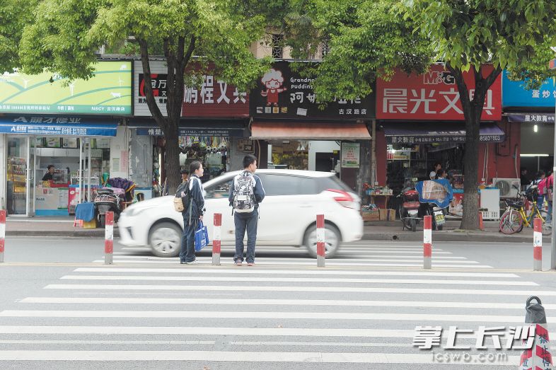 昨日下午，在马王堆小学门口，一辆白色小车从两名过马路的学生身前迅速驶过。长沙晚报记者 余劭劼 摄
