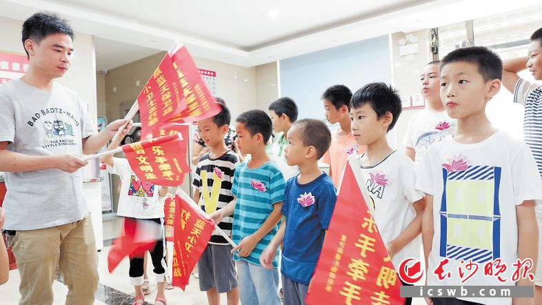 星沙街道杉仙岭社区开展“文明手拉手，礼让德先行”志愿活动，图为工作人员给小志愿者们发旗帜。陈瑶摄
